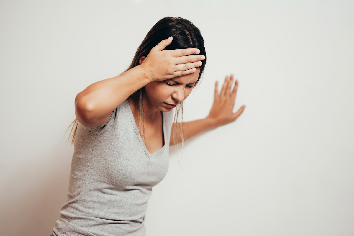 Woman suffering from dizziness with difficulty standing up while leaning on wall