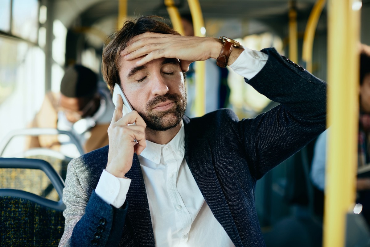 Mid adult businessman feeling displeased while talking on mobile phone and commuting by bus.