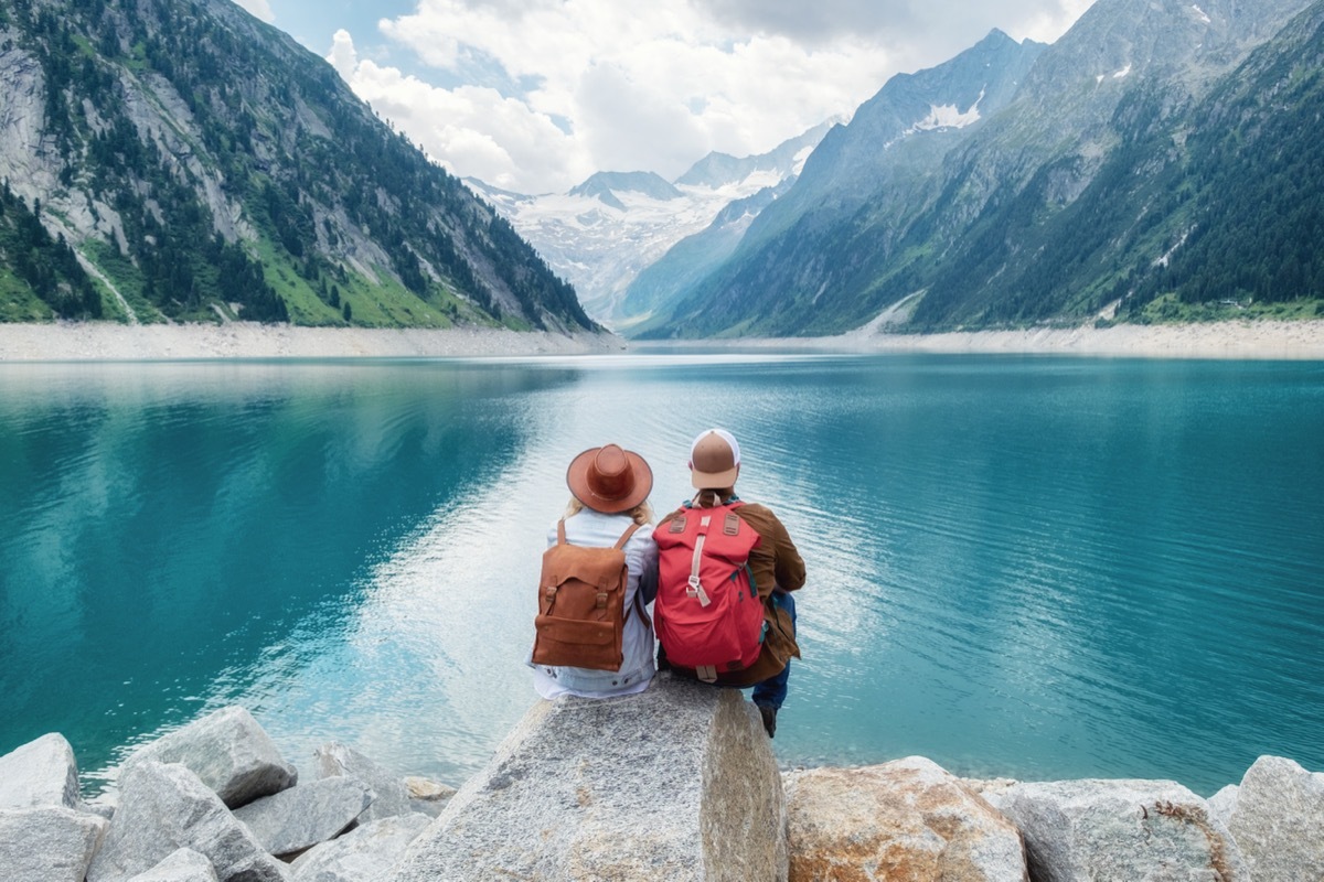 A couple in their 60's sitting by a lake surrounded by mountains.