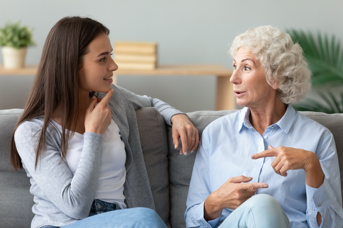 Happy grandmother chatting with granddaughter, sitting on couch at home, having pleasant conversation, positive older woman sharing news with pretty girl, grandchild, having fun together