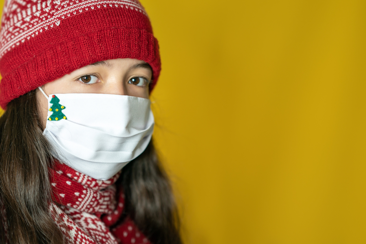 young girl wearing winter hat and covid mask with christmas tree on it