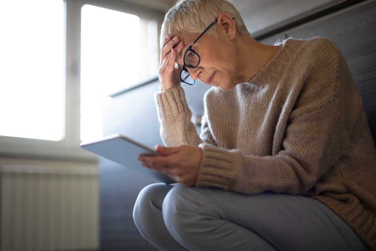 Serious senior woman using tablet computer indoors seems concerned. Mature woman trying to find a solution to financial problems