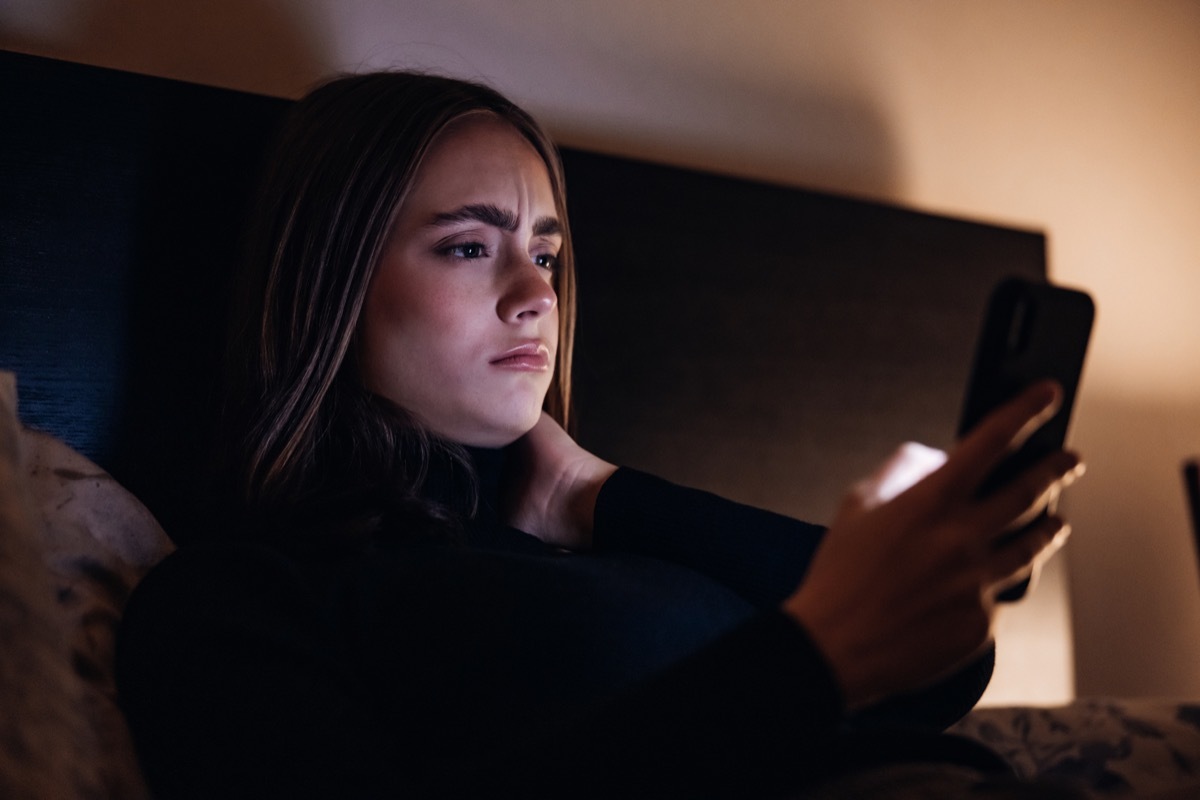 Woman laying in bed looking at phone with concerned expression