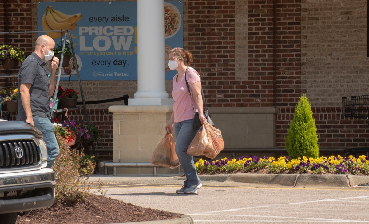 Woman walking with groceries to car with mask on