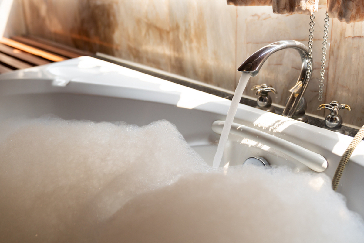 faucet on with water running into bubbles of filled up bathtub