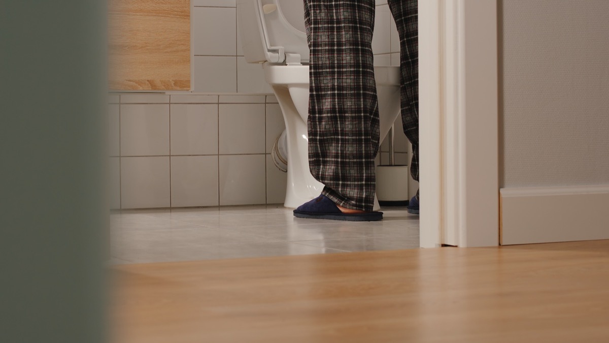 man's legs in pajamas while he pees in a toilet