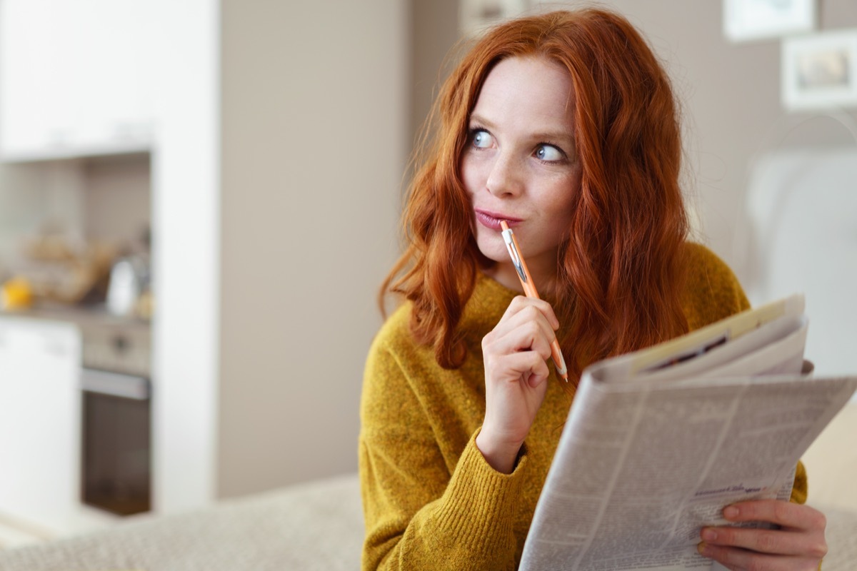 Thoughtful young woman doing a cryptic crossword puzzle in a newspaper