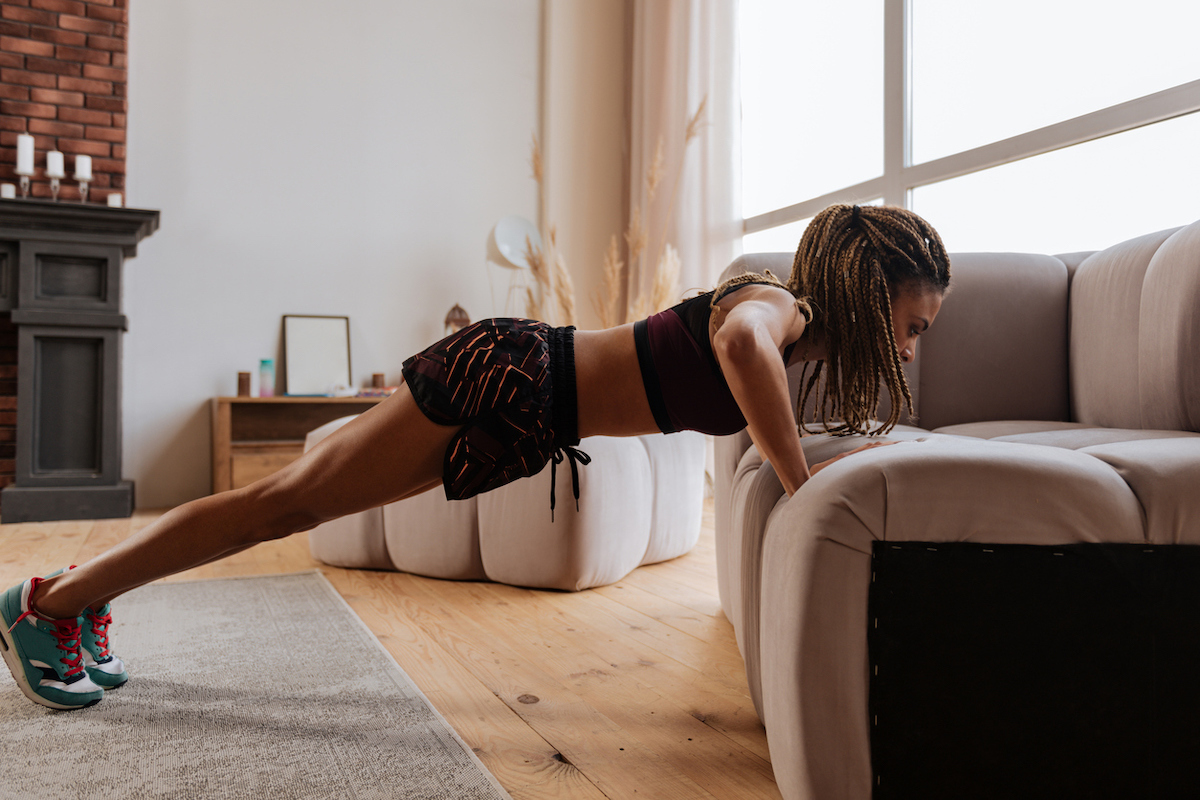 Active black woman doing pushups on sofa at home