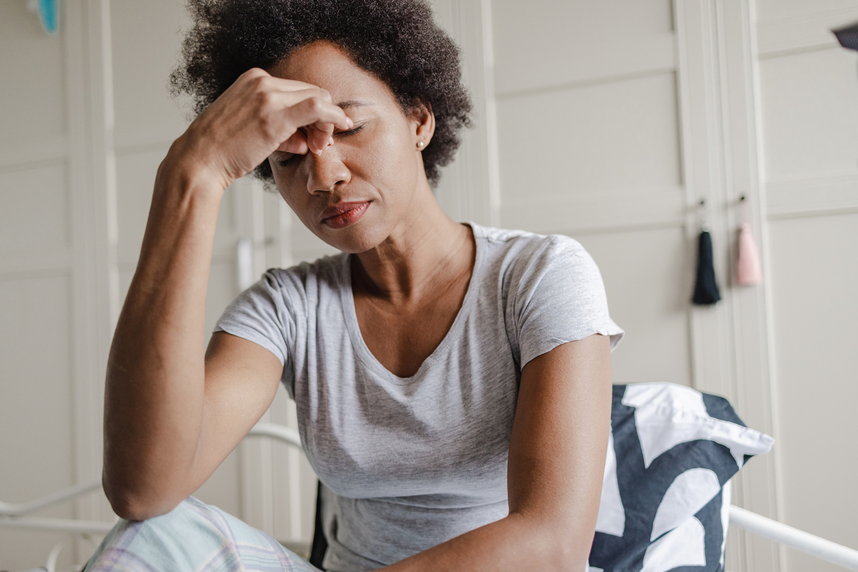 Woman sitting on a bed rubbing her eyes.