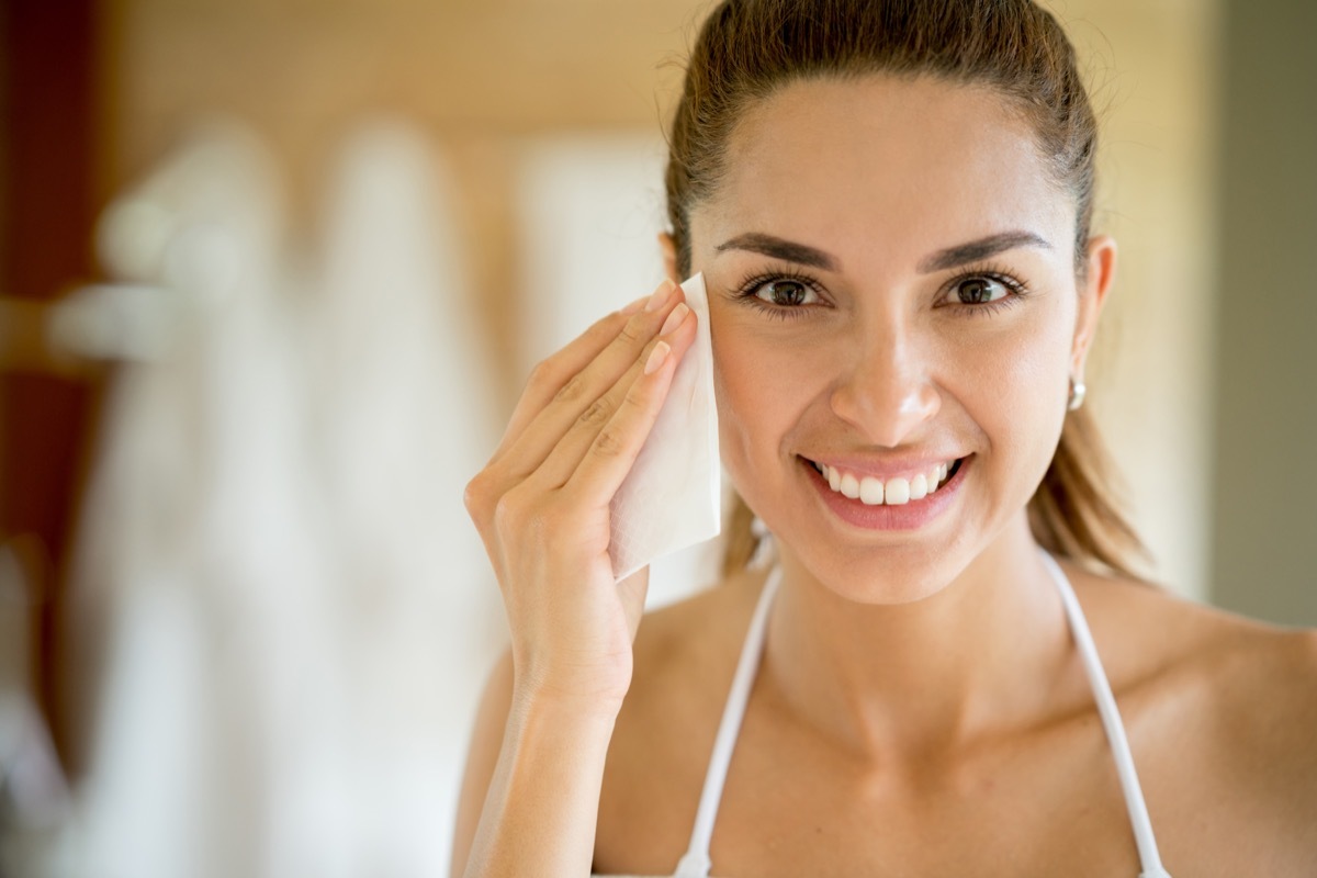 portrait of a beautiful woman cleansing her face with a pad and removing her make up while looking at the camera smiling