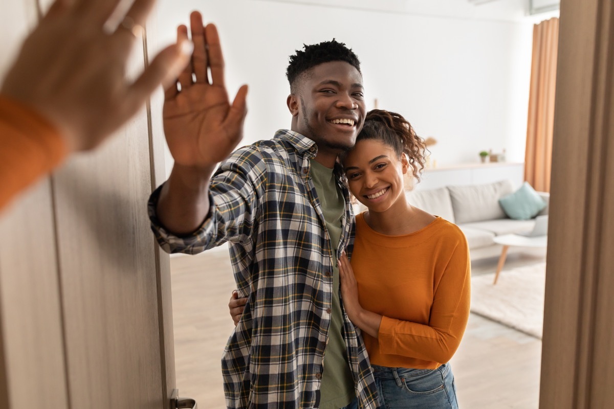 happy couple standing in opened doors of their house waving goodbye to guests