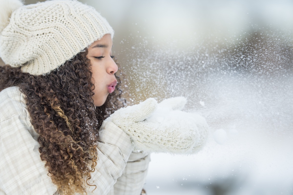 girl blowing snow with gloves on