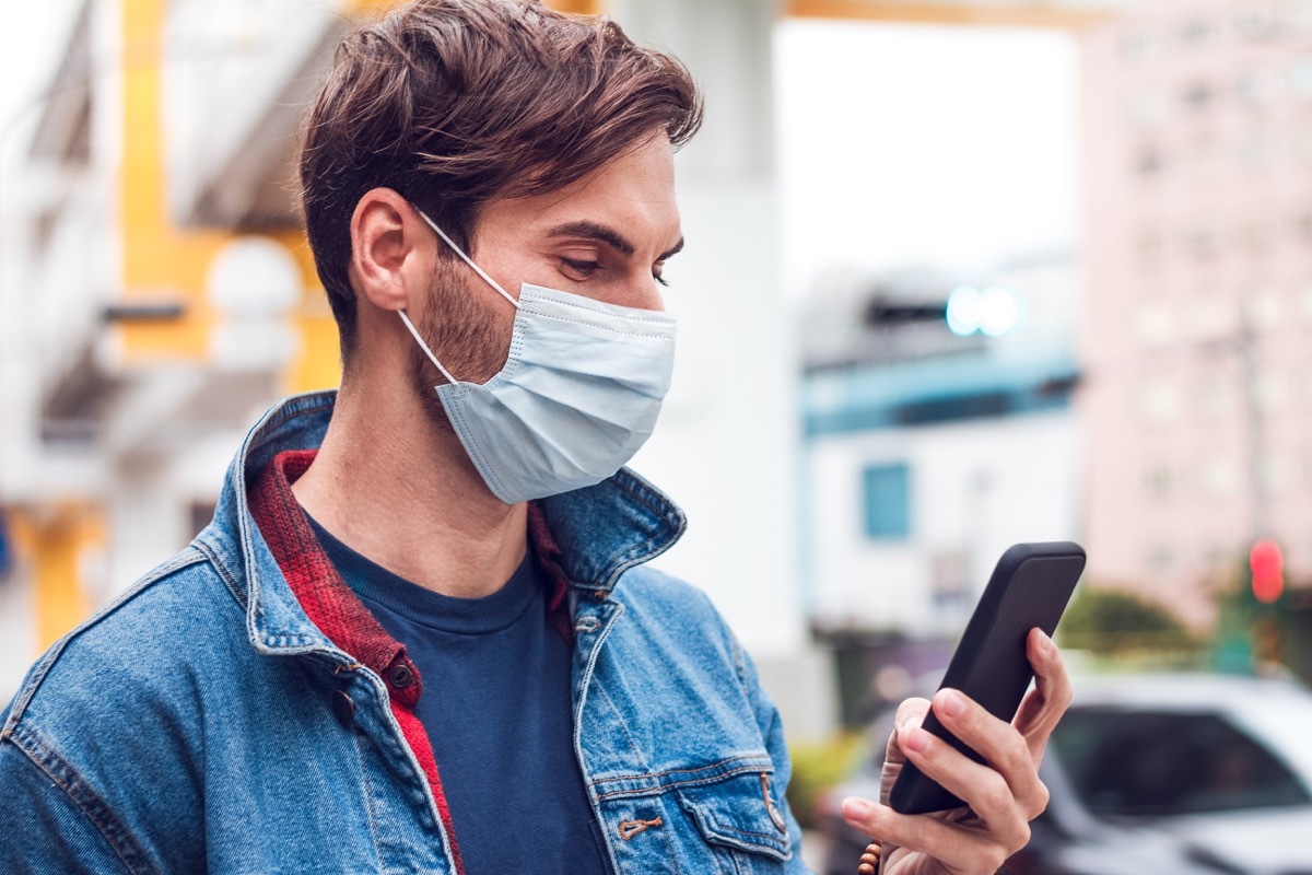 man with a mask looks at his phone