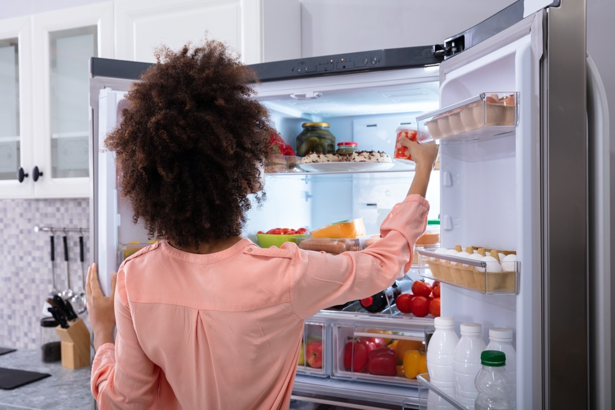 woman in pink shirt with dark curly hair opening double door fridge