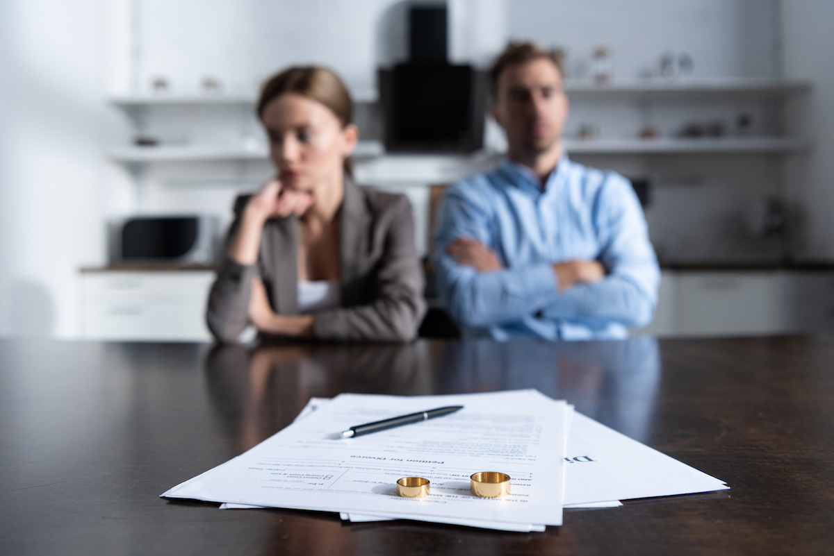 An unhappy couple sitting at a table with divorce documents and their wedding bands.