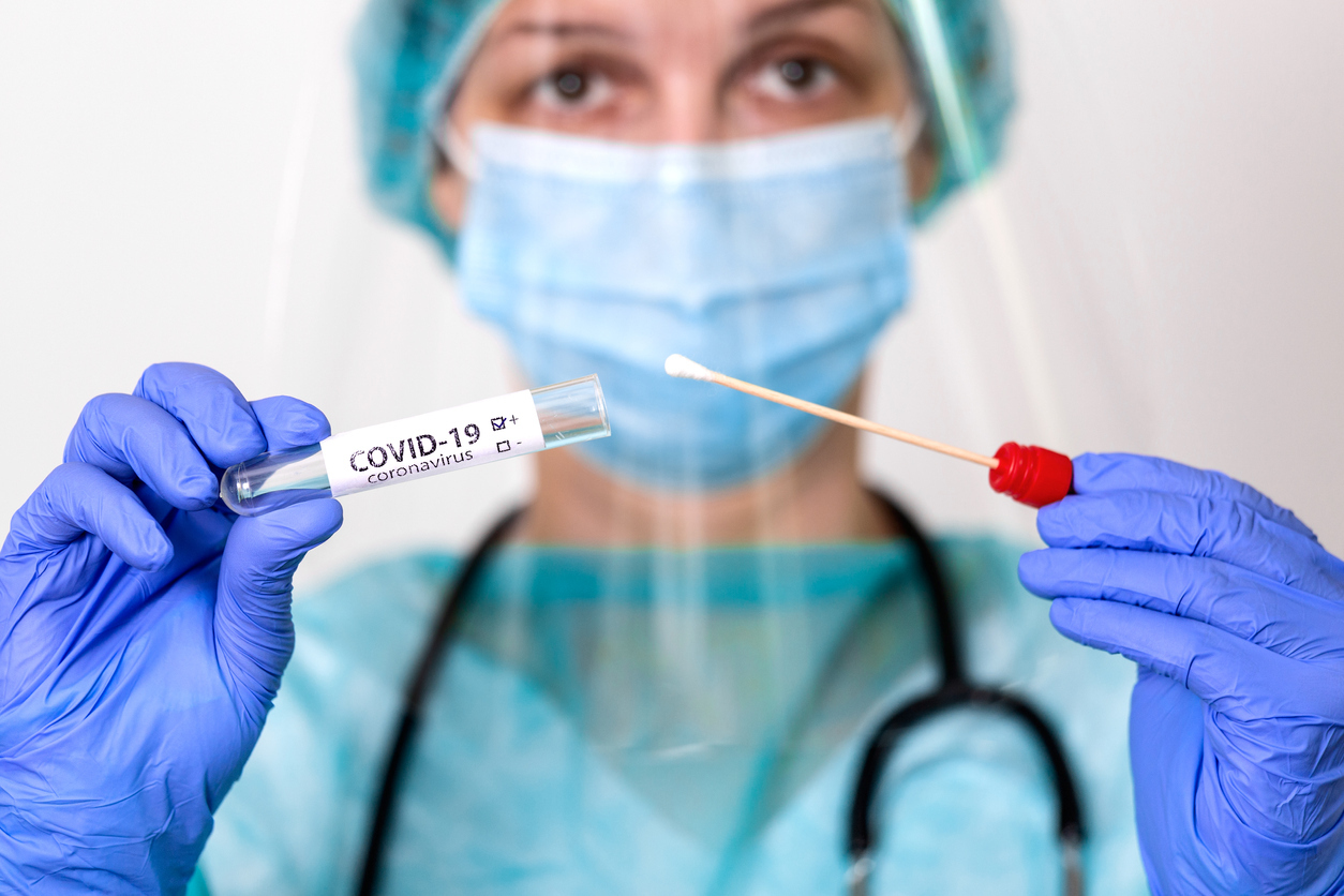 A healthcare working wearing PPE holding a nasal swab and tube for a coronavirus test.