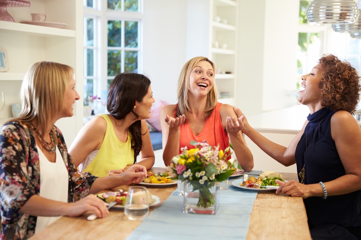 four women laughing and eating at a dinner party