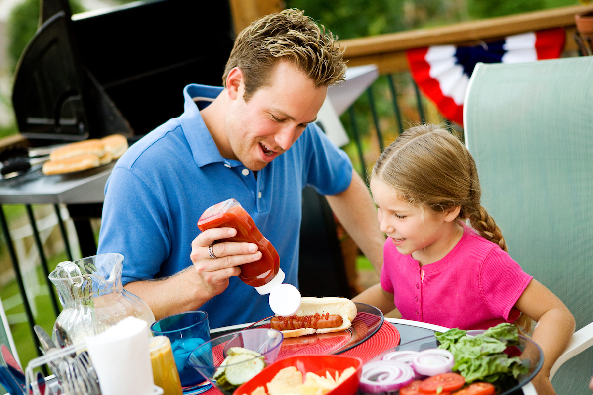 Dad putting ketchup on daughter's hot dog