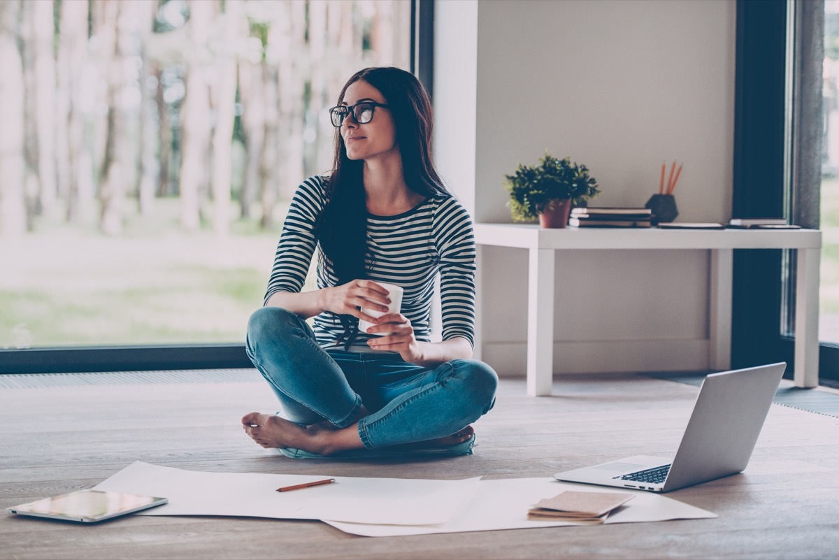 woman sitting on the ground holding a cup of coffee surrounded by papers containing inspirational quotes