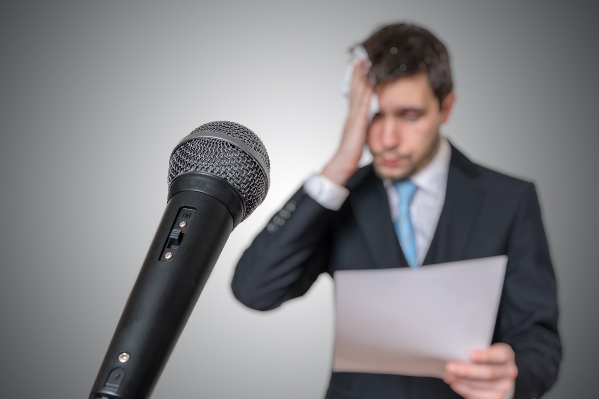 man holding a piece of paper and wiping sweat in front of microphone