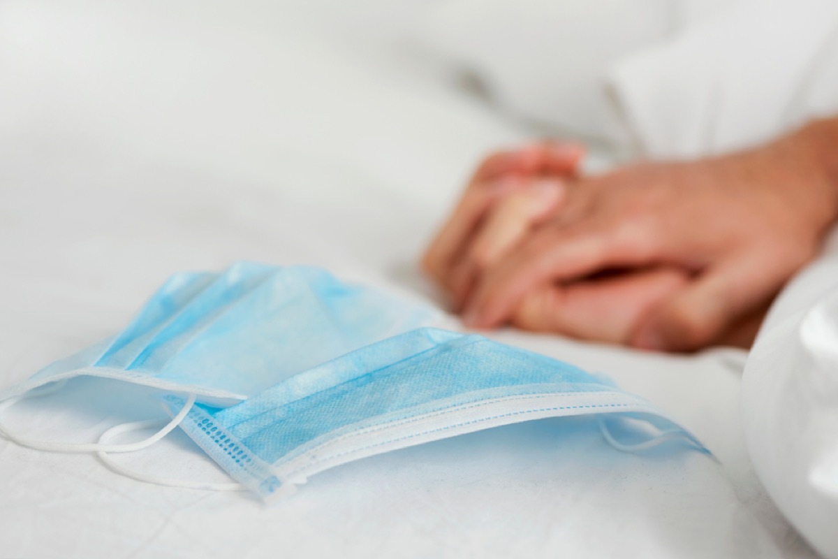 close up of surgical face masks next to hands clasped in bed