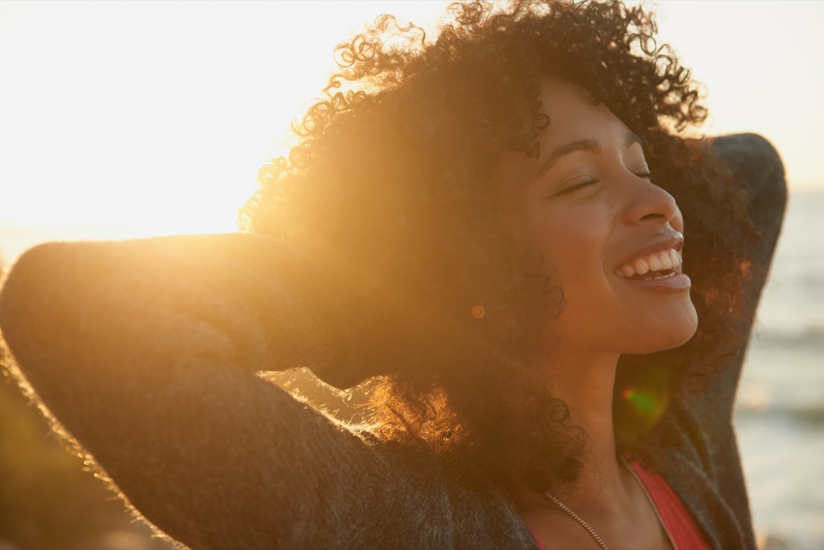 woman with her hands behind her head and eyes closed, raising her face to the sun