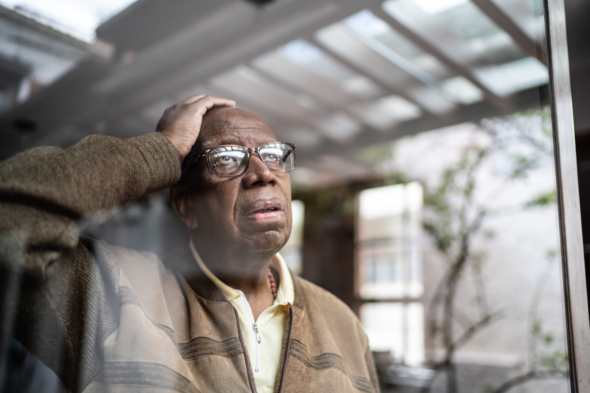 Worried senior man looking through the window at home