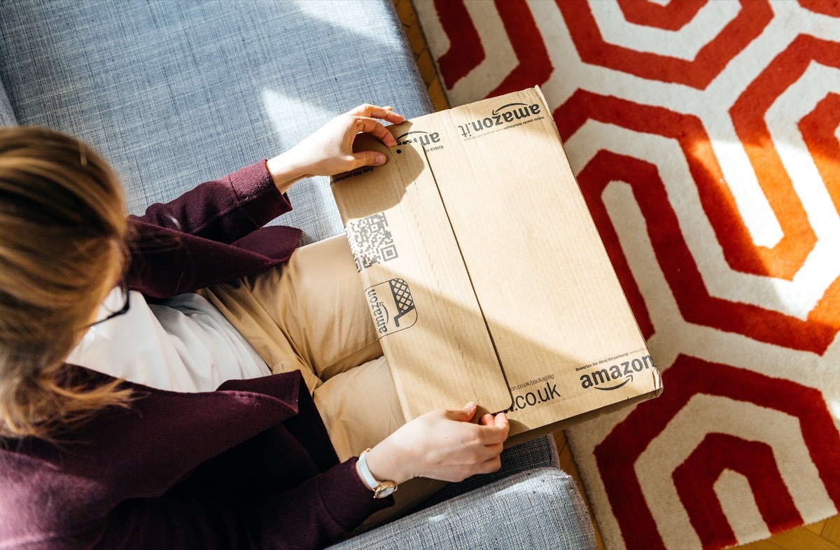 PARIS, FRANCE - APR 24 2017: Living room view from above of woman unpacking unboxing Amazon cardboard box logotype printed cardboard box side. Amazon Inc is the an American e-commerce shopping company