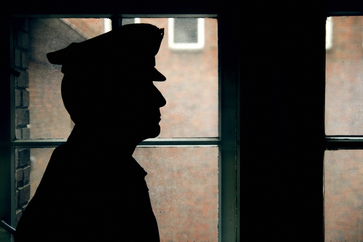 warder's silhouette, prison walls outside the window.