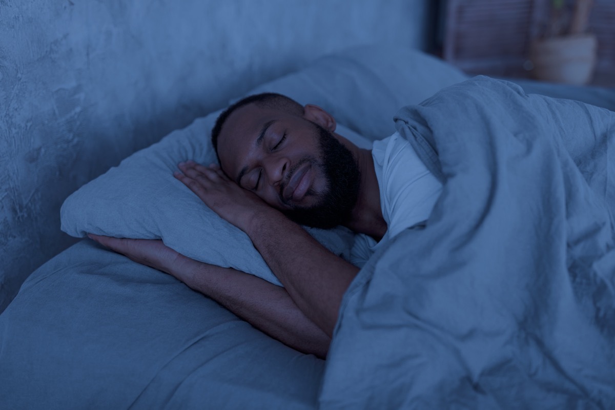 Healthy Sleeping Concept. Portrait of happy young well-slept man lying in bed with closed eyes, resting in bedroom on the side in the dark night.