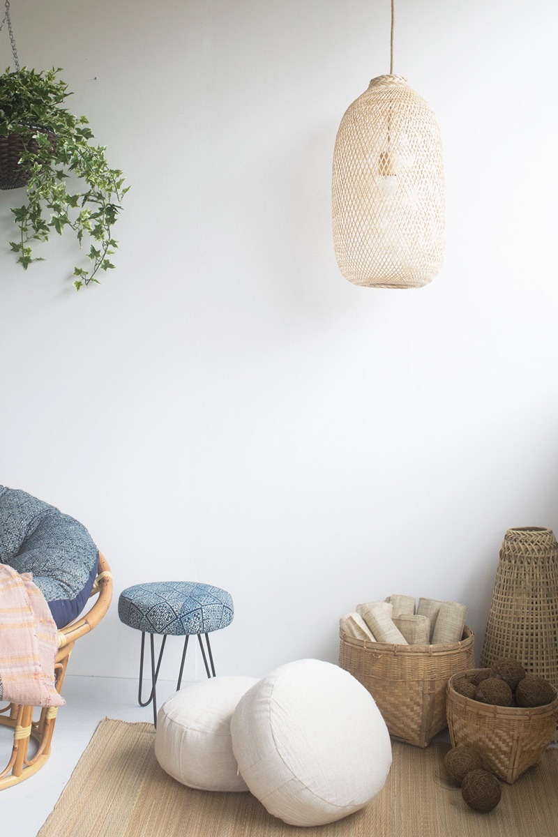 brown woven pendant lamp hanging over two white cushions, a blue stool, woven baskets, and a blue papasan