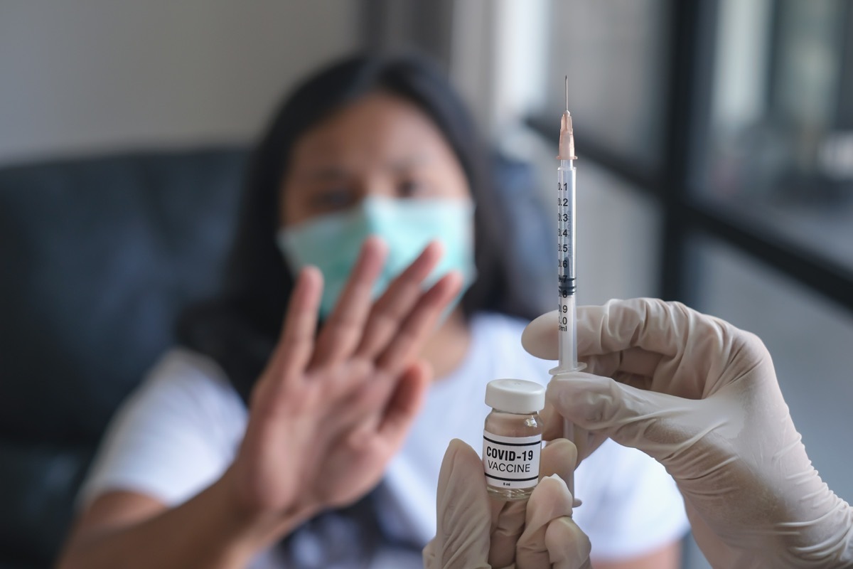 Close-up shot of an unrecognizable doctor holding a syringe and covid-19 vaccine in front of a woman who refusing the Covid-19 vaccine.