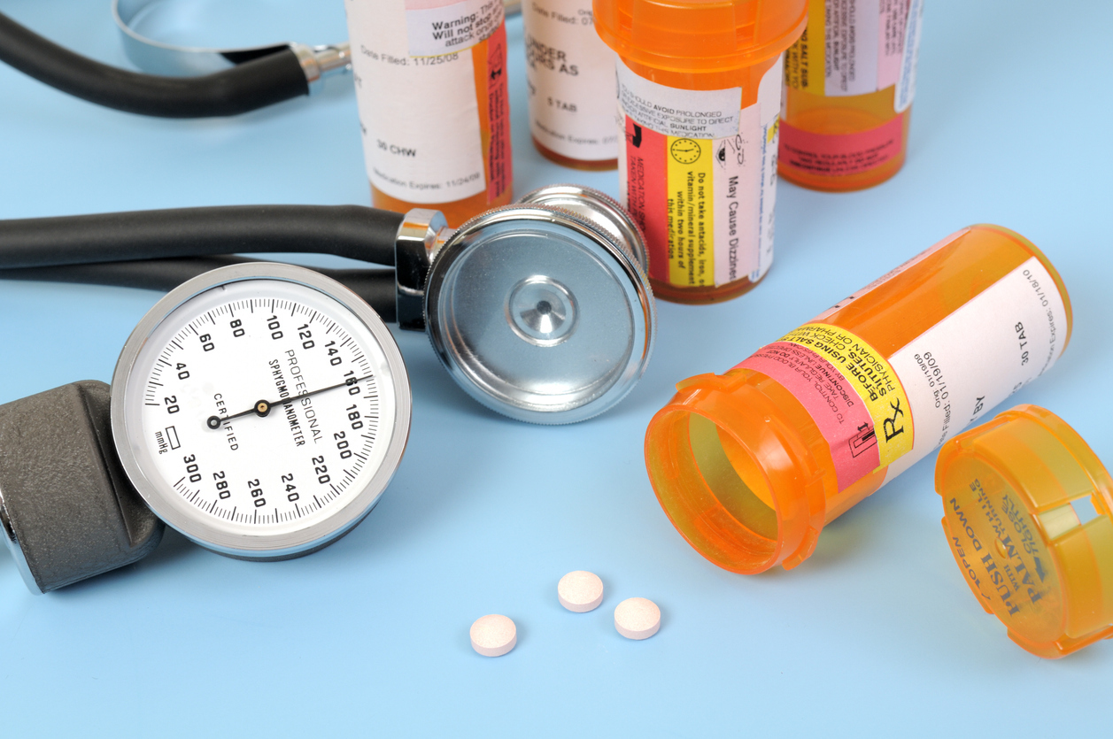 A blood pressure gauge showing high blood pressure, stethoscope, and medicine bottles, and pills.