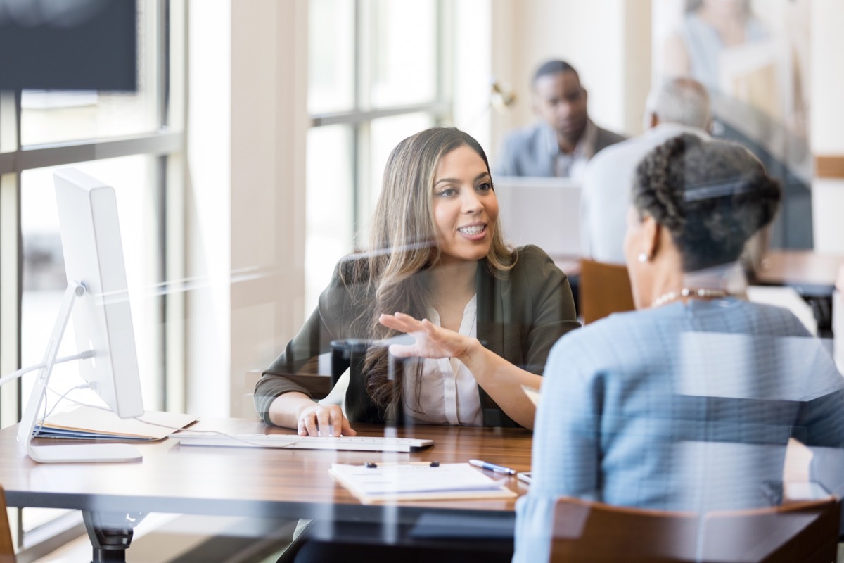 A mid adult female bank employee gestures as she explains banking services to a female customer.