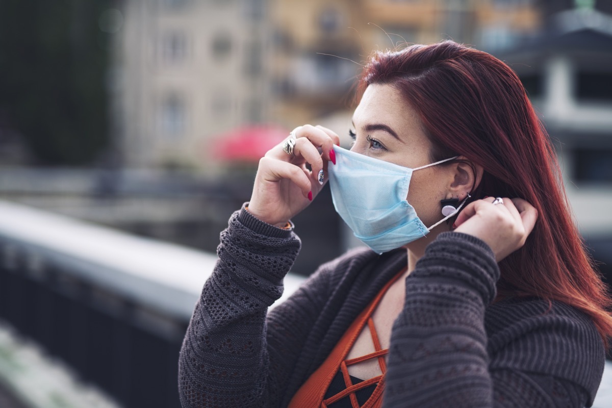 Side view of woman puts on protective face mask outdoor.